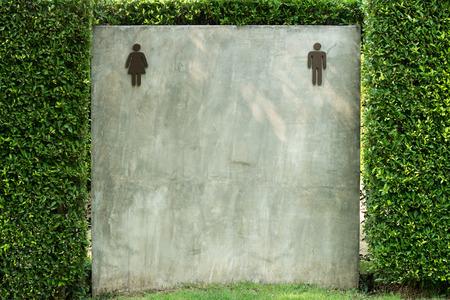 A unisex public toilet sign is on a grey cement wall and green leaf.の写真素材