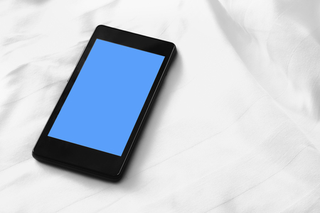 cellphone on white bed sheetsの写真素材