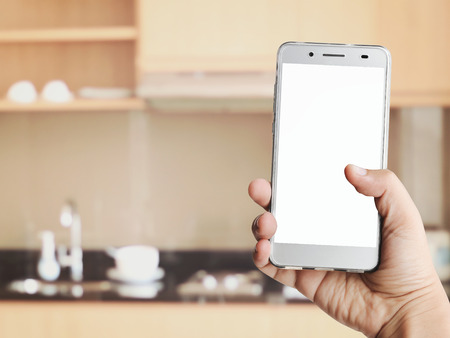 hand holding phone with white blank screen on blur kitchen backgroundの写真素材