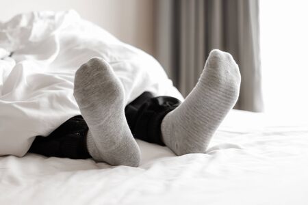 foot in gray socks relaxing on the white bedの写真素材