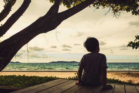 child sitting and looking at the beach under the treeの写真素材