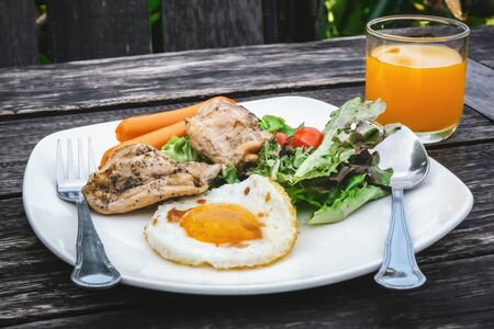 grilled chicken fried egg sausage and salad with juiceの写真素材