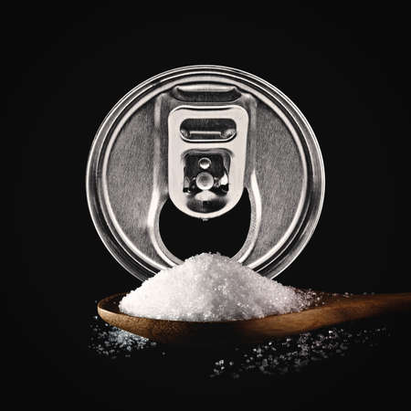 sweetened beverages. carbonated can and sugar in the spoon on black background. unhealthy food...