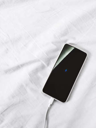 smartphone charging on the wrinkle white bed sheet. low battery mobile phone.の写真素材