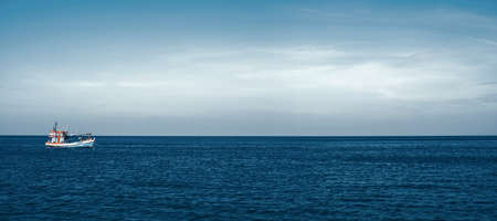 A fishing boat floats alone in the calm sea. The sky background above the horizon for copy space. Ocean nature landscape. The vessel is on the water.の写真素材