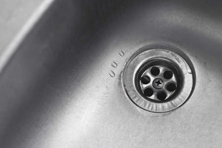 Water drop down on stainless steel kitchen sinkhole. top view sewer. Drain in the washbasin. Household plumbing. cleaning and hygiene concept.の写真素材