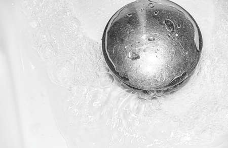 Water drain down on sewer in white washbasin. Household plumbing. Cleaning and hygiene concept.の写真素材