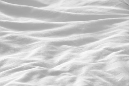 Wrinkled white bedsheet background. Cozy fabric texture surface. Untidy duvet backdrop. Relaxation and comfortable accommodation.の写真素材