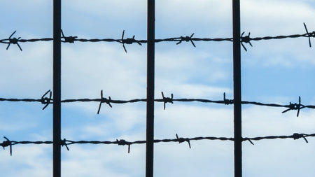 Barbed wire fence against blue sky background. Prison cage area. Obstacle and boundary concept. Country border.の写真素材