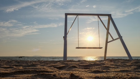 Sunset by the sea and beach. Swing with sky and water view.