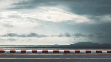 Empty asphalt road along the coastline with sea and cloudy sky in overcast weather. Minimal landscape background for travel, journey, or road trip concept.の写真素材