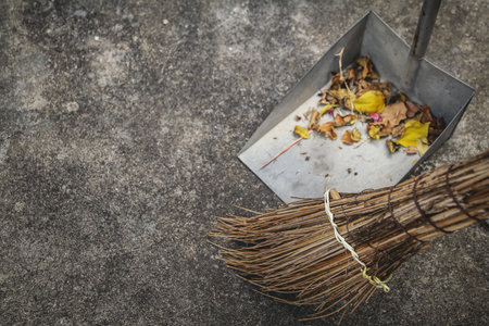 Broom cleaning fallen leaves into a dustpan on concrete ground, concept of cleanliness, housework and outdoor maintenance.の写真素材