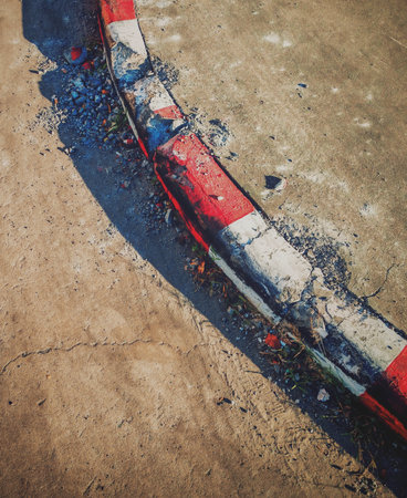 Damaged red-and-white painted curb with cracks, chipped concrete, and scattered debris. Urban sidewalk background. Old streets rough and grunge.の写真素材