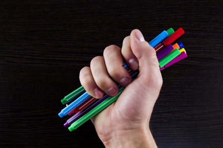 Multicolored markers in a hand on a dark background table conceptの写真素材