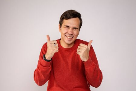 A young guy in a red sweater laughs. Portrait on gray backgroundの写真素材