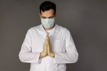 The doctor prays to God with a request that the coronavirus will stop its action on the planet. Photo on a grey backgroundの写真素材