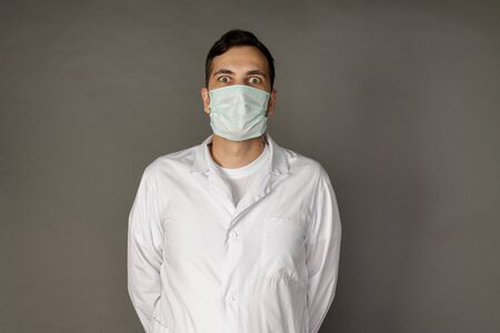 Portrait of a doctor in a medical gown and protective mask. Photo on a grey backgroundの写真素材