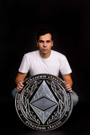 A man with a coin in his hands ethereum classic stands in the background. Photo on black backgroundの写真素材