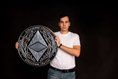 A man with a coin in his hands ethereum classic stands in the background. Photo on black backgroundの写真素材