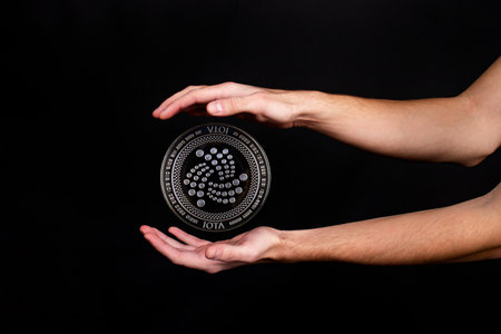 Elements of the IOTA cryptocurrency fall on the hand. Photo on a black backgroundの写真素材