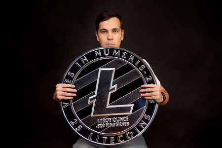 A man holds a litecoin coin in his hands as a symbol of technology. Image on black background