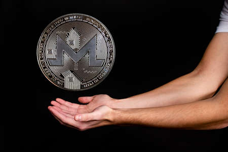 Monero coin and a man's hand on a black background. A symbol of technology and a new means of currency settlementの写真素材