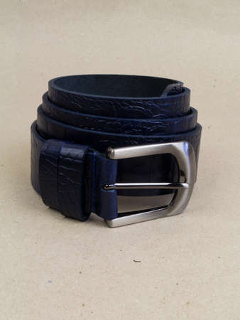 A leather belt with a clasp lies neatly on the table. background light paper