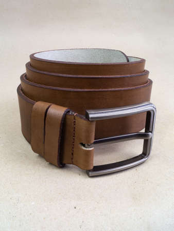 A leather belt with a clasp lies neatly on the table. background light paperの写真素材