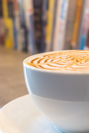 Cup of coffee latte art on wooden table with bookshelf backgroundの写真素材