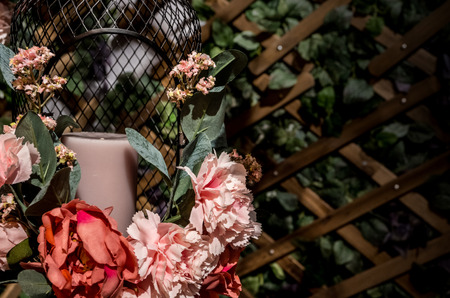 A white candle in decorated bird cage from artificial flower with blurred vertical garden backgroundの写真素材