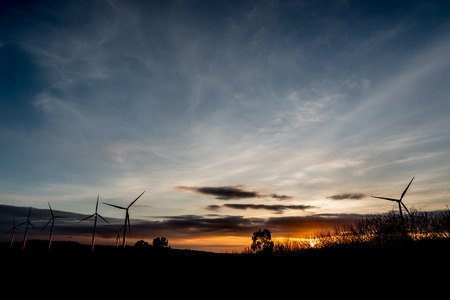 Silhouette of wind turbines on the mountain at sunset. Sunlight through the dark clouds with...