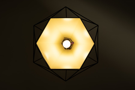 Modern lamp hanging down from ceiling in the dark background. Minimalist chandelier with glowing warm light from bulb. - Imageの写真素材