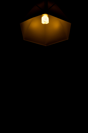 Modern lamp hanging down from ceiling in the dark background. Minimalist chandelier with glowing warm light from bulb. - Imageの写真素材
