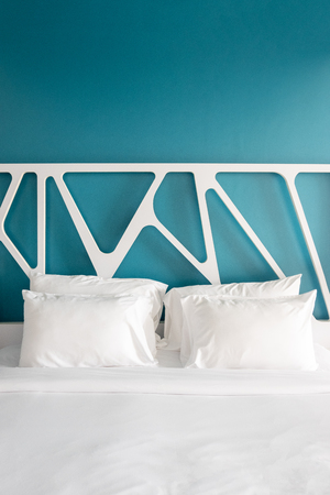 Close up white bedding sheets and pillow in modern bedroom. Front view of empty bed with sunlight.