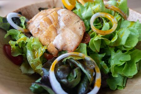 Salad with grilled chicken breast and orange sauce on wooden bowl. Close up of healthy summer food.