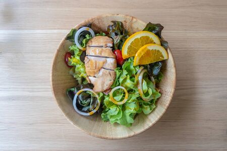 Salad with grilled chicken breast and orange sauce on wooden bowl. Top view of healthy summer food.の写真素材