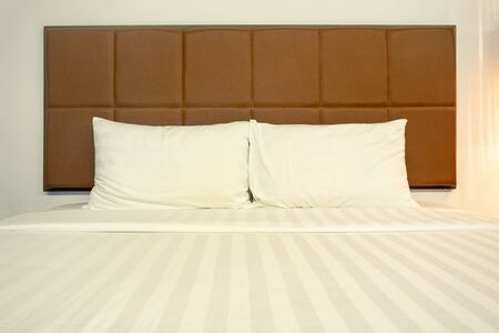 Close up white bed sheets and pillows in hotel or apartment. Front view of clean bedroom with warm...