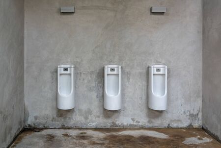 White ceramics urinals in loft toilet. Grunge public restroom with concrete wall.の写真素材