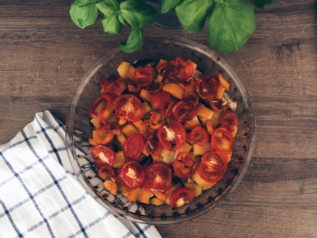 Roasted eggplant, tomatoes and yellow bell pepper in a glass pan on a wooden table.の写真素材