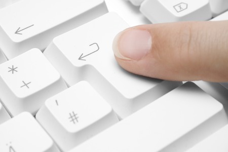 Forefinger pressing the enter button on a white keyboard.