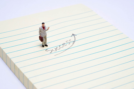 Miniature businessman on paper writting text "success" isolated on white background.の写真素材