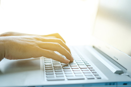 Hands of a man typing on a computer keyboard with a warm light.