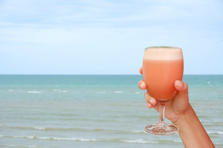 Closeup fruit juice in glass in hand on sea background.の写真素材