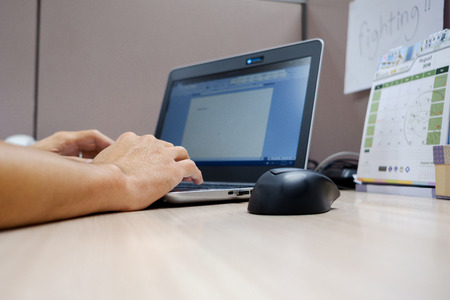 Hands of a man typing on a computer keyboard on the table.