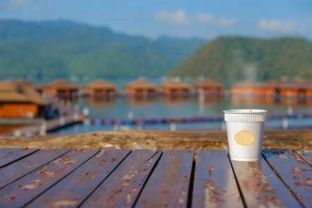 Closeup a hot coffee on plank and view house in sea background.の写真素材