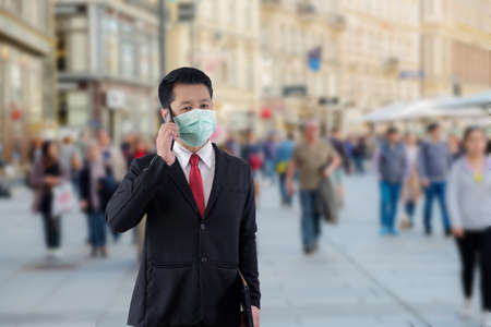 Businessman wears mask and he is talking the phone when he is going to a place with many people.の写真素材