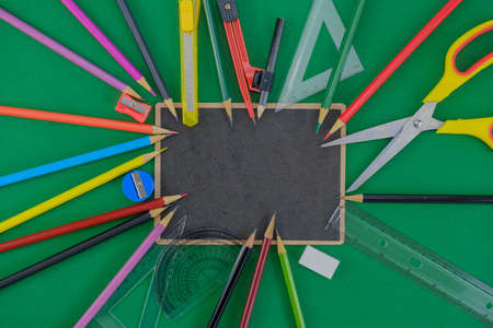 Many school supplies put on black board on green background.