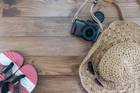 Top view the glasses put on the hat near a camera and there is a slipper on wooden background.の写真素材