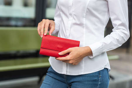 Girl in white holds a red wallet in her handの写真素材