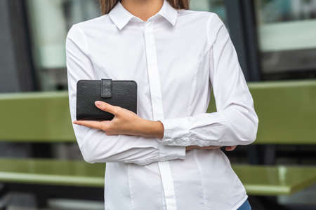 Girl in white holds a black wallet in her handの写真素材